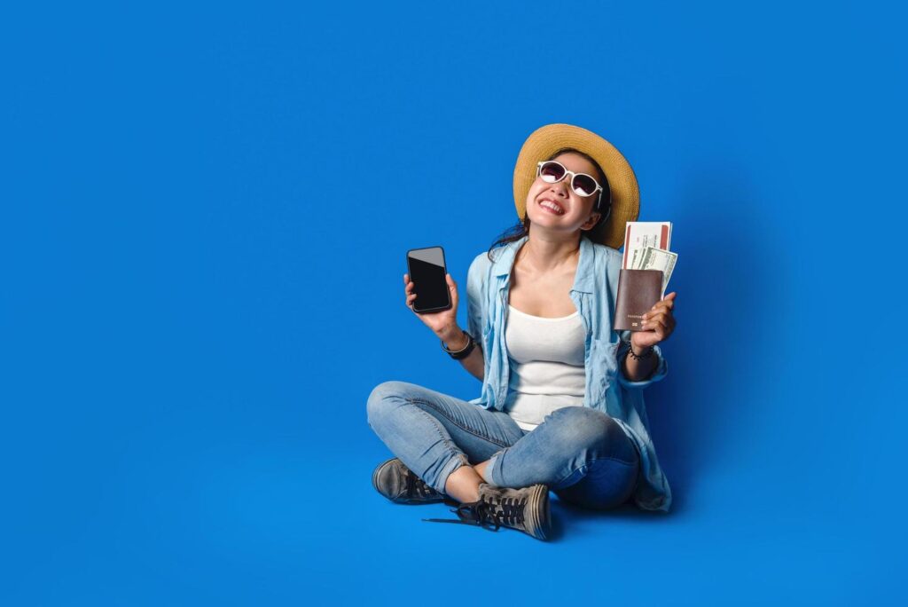 Traveler girl in a blue dress is smiling happy with a cheerful face and holding passport with holding mobile phones in the hand, on blue color background. concept travel Stock Free