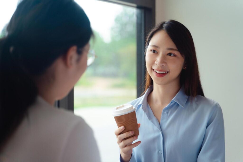 Two business women are talking and one of them is holding a coffee cup in the office Stock Free