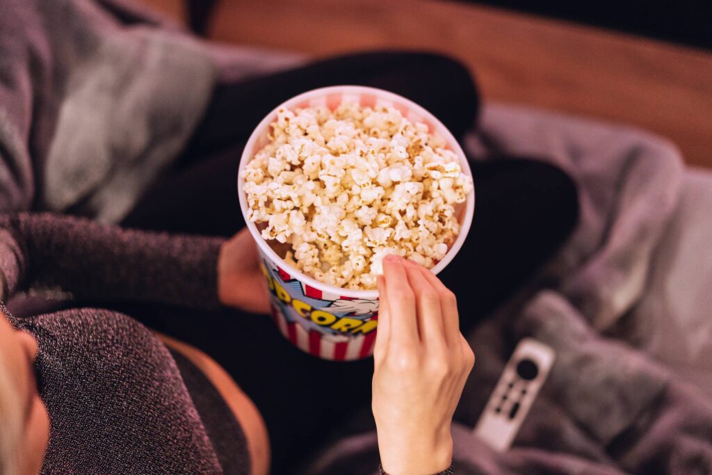 Woman Eating Popcorn while Watching TV at Home Free Photo