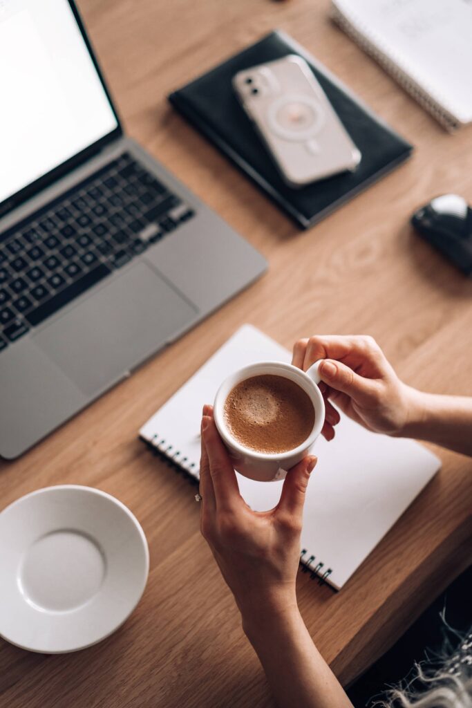 Woman Holding a Cup of Coffee while Writing and Working Free Photo