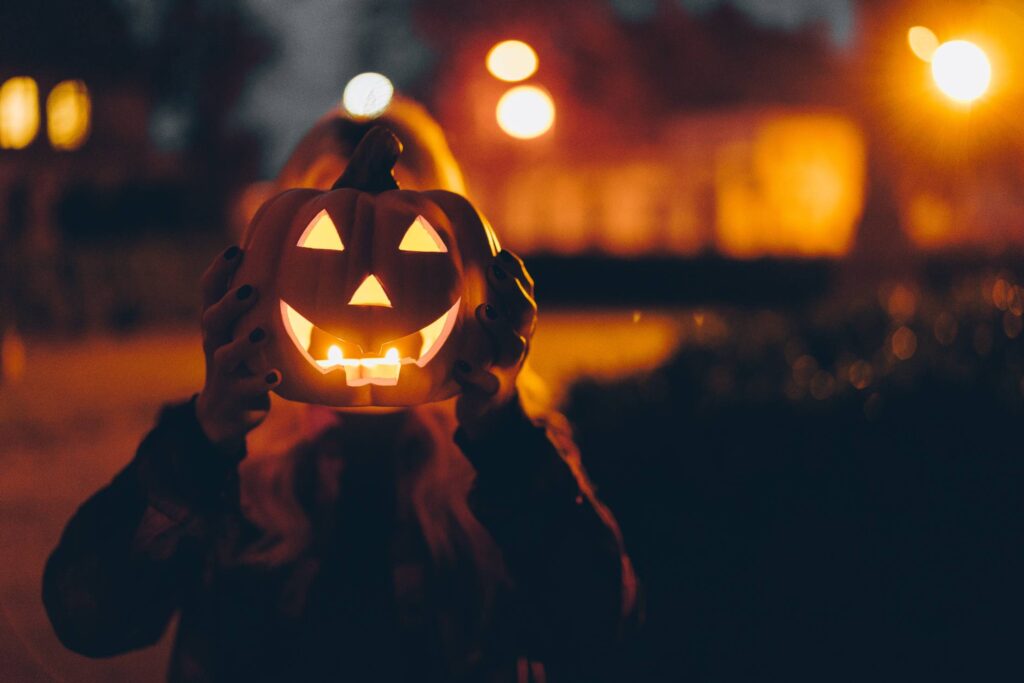 Woman Holding a Halloween Pumpkin in front of her Face at Night Free Photo