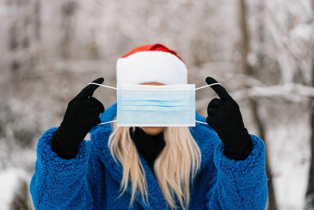 Woman in Santa Hat Holding a Face Mask in Front of Her Face Free Photo