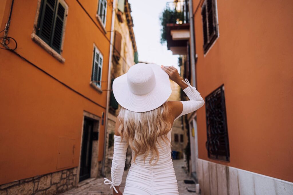 Woman in White Summer Hat Walking Down The Old Street Free Photo