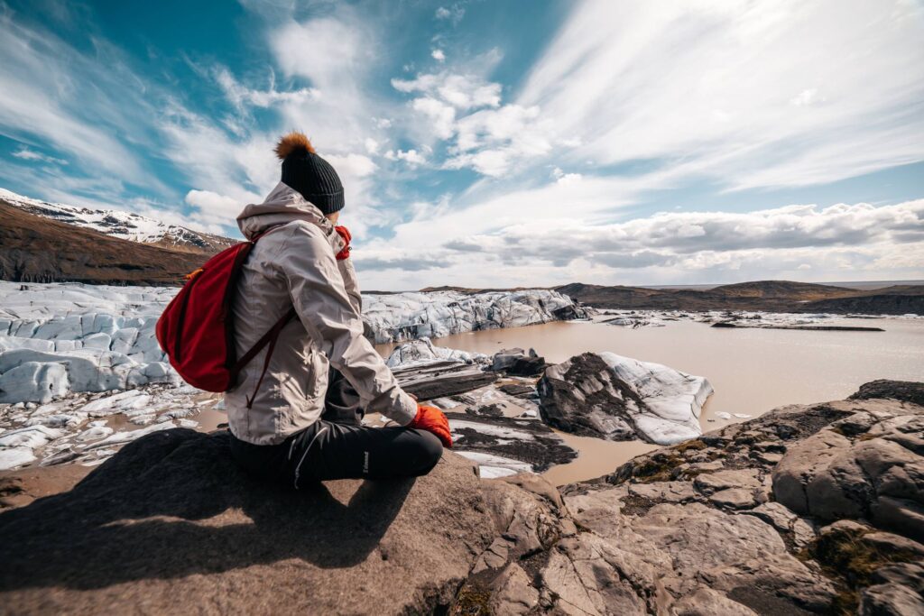 Woman in Winter Clothes Sitting on a Rock Looking at Icelandic Glacier Free Photo