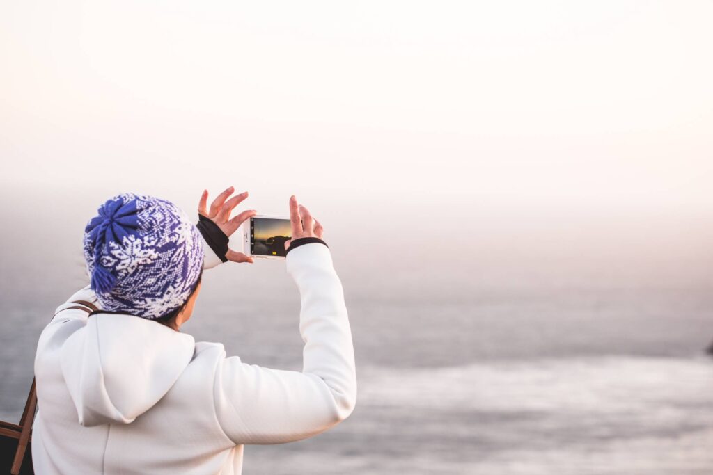 Woman in Winter Hat Taking a Picture of Endless Ocean Free Photo