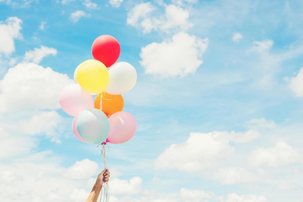 Woman Lifestyle concept woman hand holding a bunch of colored balloons with blue sky. Stock Free