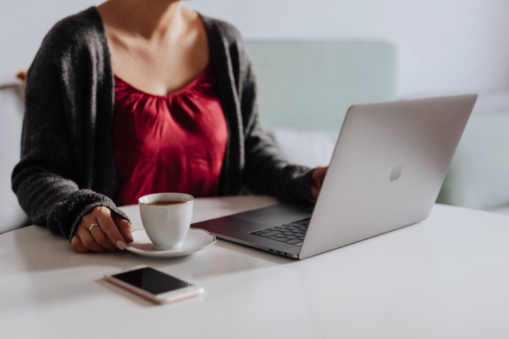 Woman Sitting at a Table with a Cup of Coffee and Working on a Laptop Free Photo