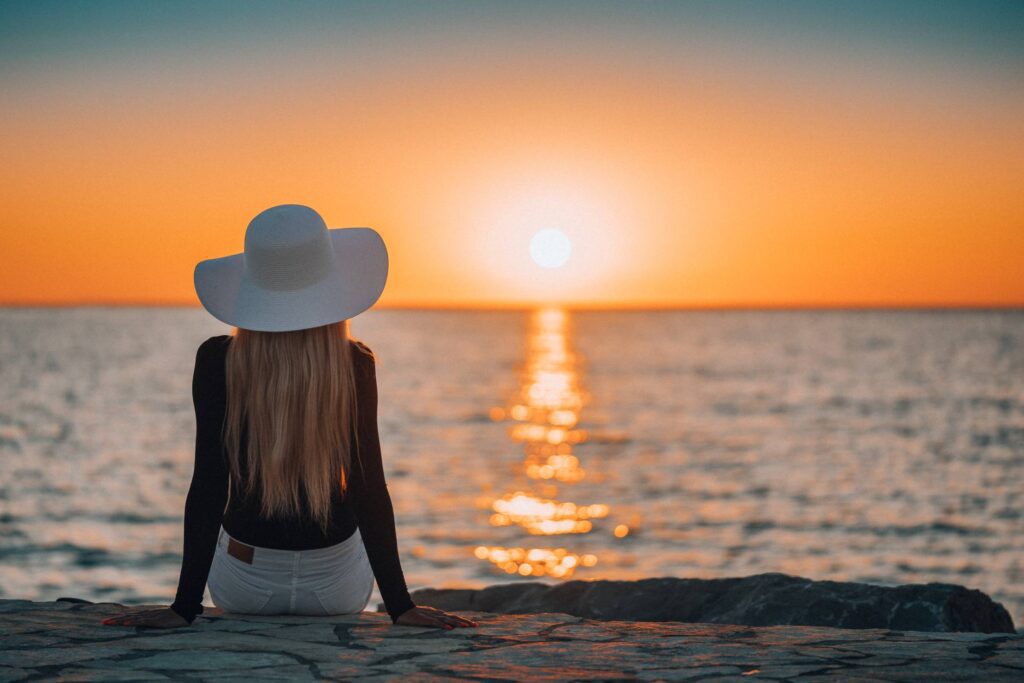 Woman Sitting on a Rocky Shore by the Sea and Watching Sunset Free Photo