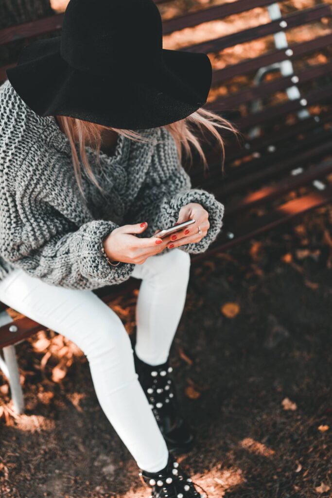 Woman with a Hat Sitting on a Bench and Typing on Her Mobile Free Photo