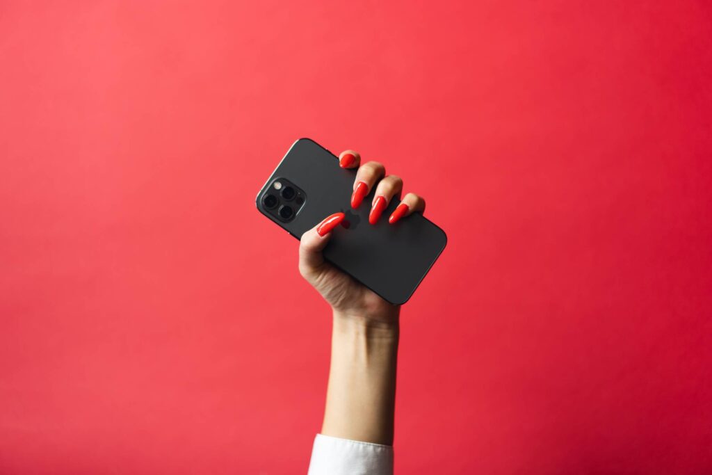 Woman with Red Nails Holding a Smartphone on Red Background Free Photo