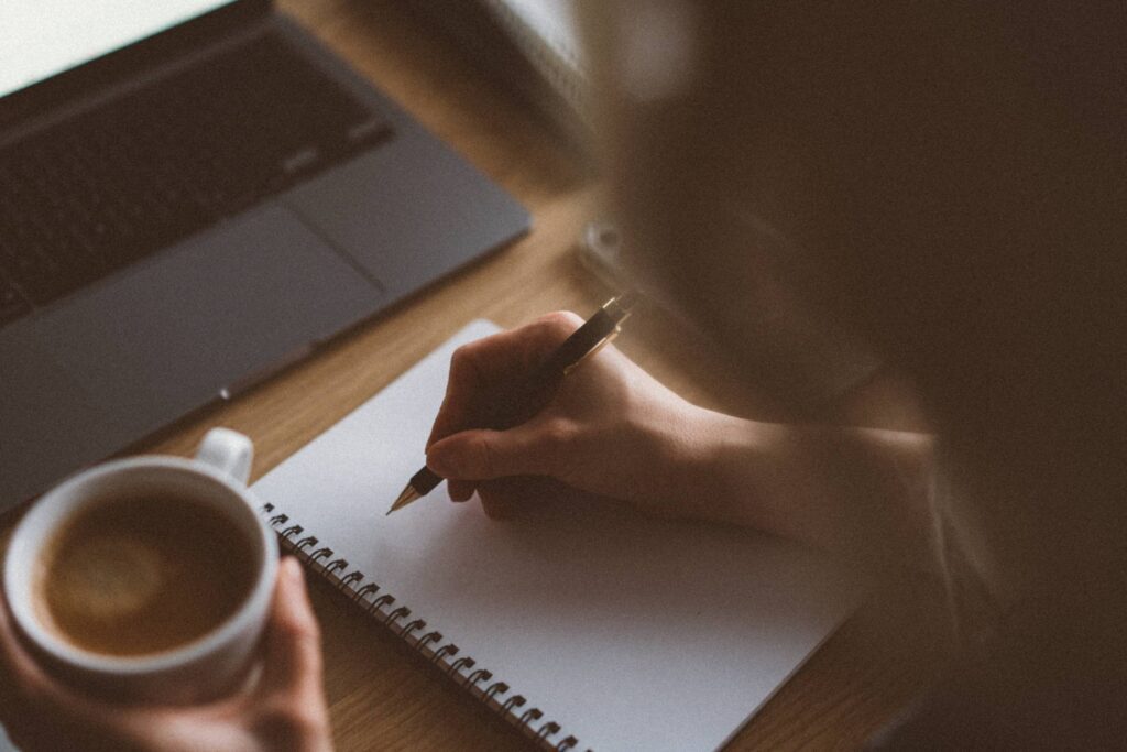 Woman Writing in Diary and Holding a Cup of Coffee Free Photo