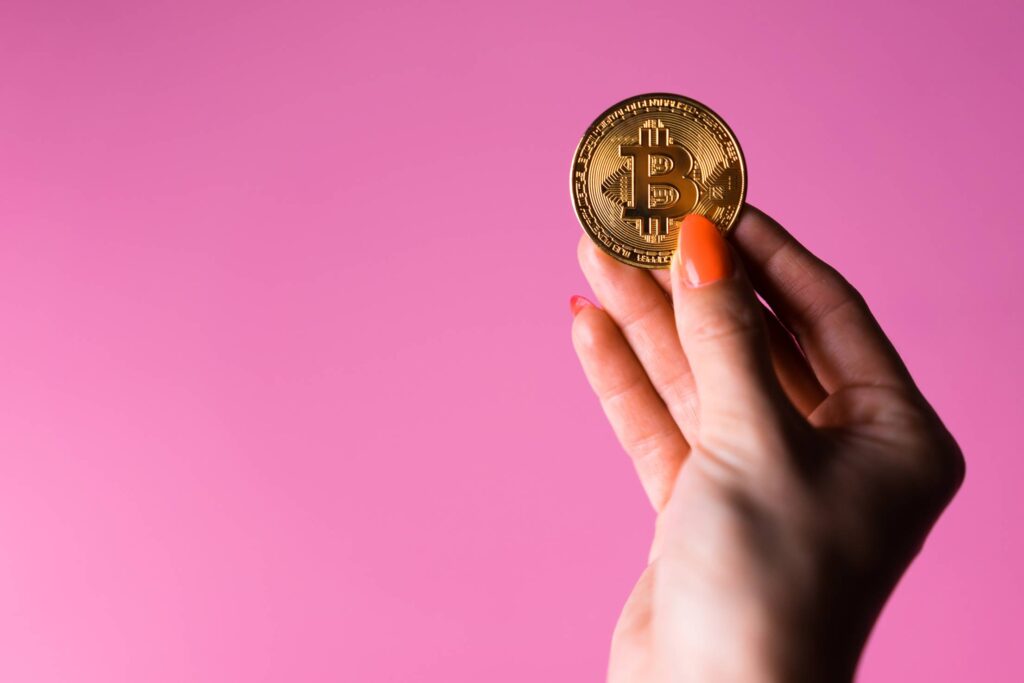 Woman’s Hand with a Glowing Gold Bitcoin on a Pink Background Free Photo