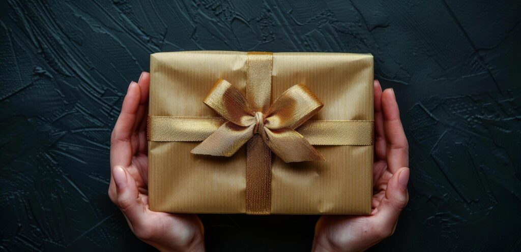 Womans Hands Holding a Gold Gift Box With a Bow on a Black Background Stock Free