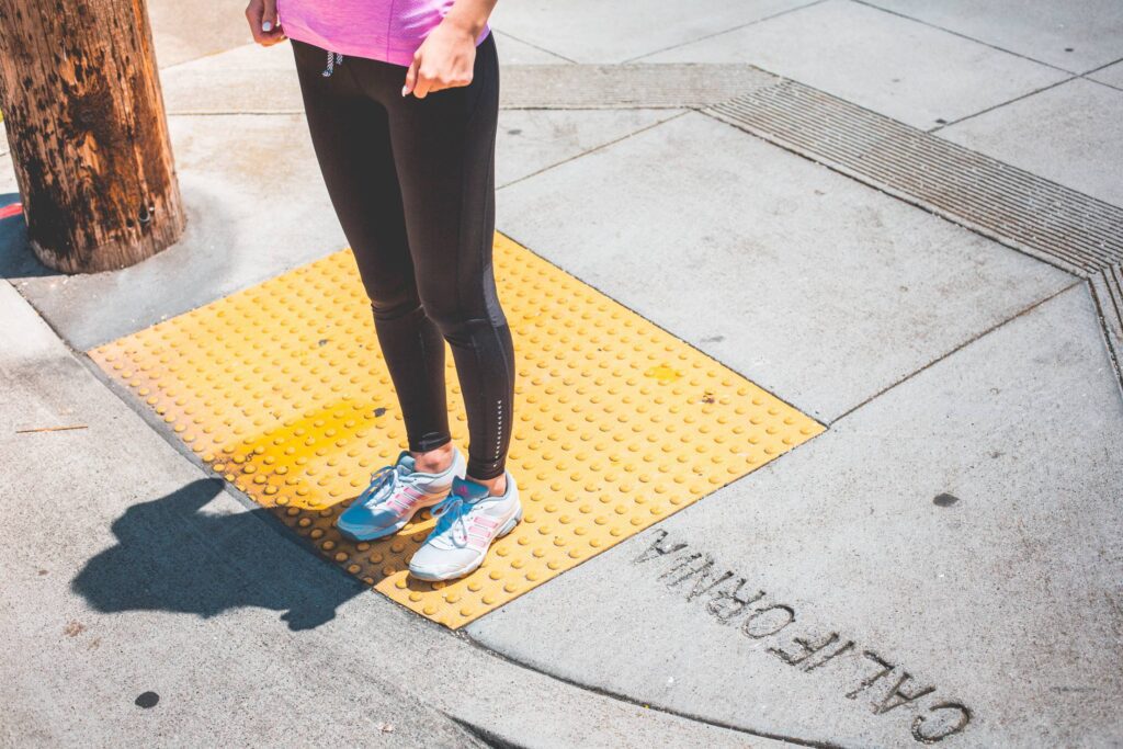 Young Female Jogger Waiting at the Edge of a Zebra Crossing Free Photo