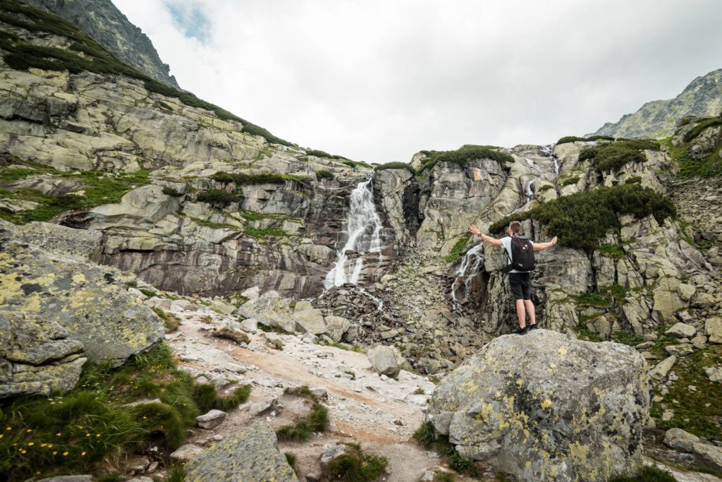 Young Man with Open Arms under Big Waterfall Free Photo