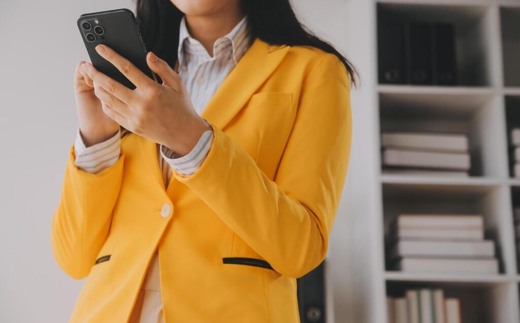 Young smiling business woman using smartphone near computer in office, copy space Stock Free