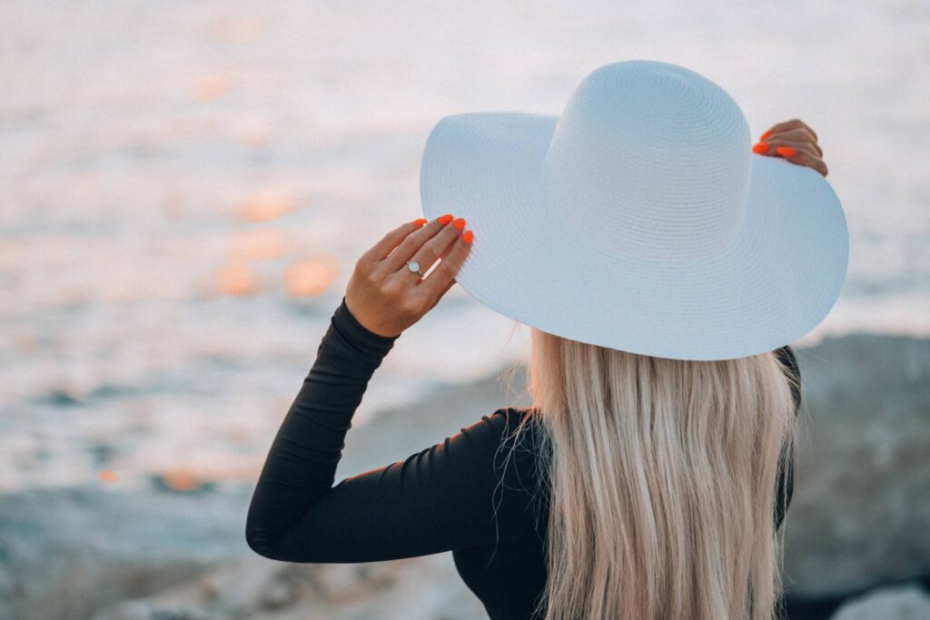 Young Woman in White Hat Enjoying Evening Golden Hour by the Sea Free Photo