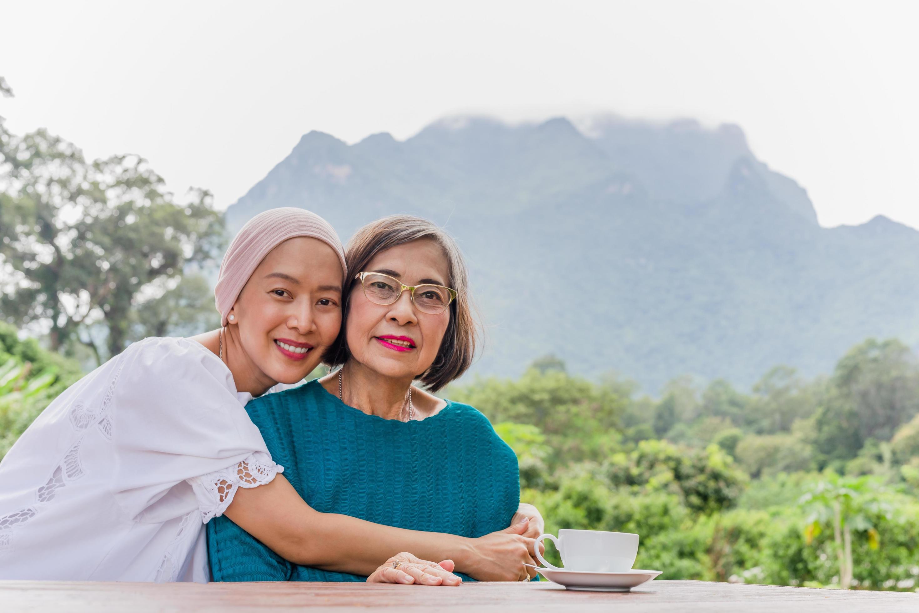 Senior mother and adult daughter are hugging traveling together with mountain view in background. Stock Free