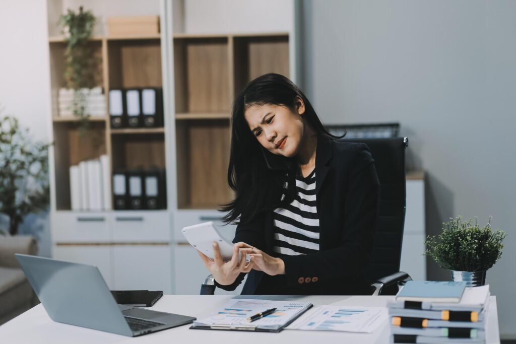 Young Asian businesswoman using a calculator to calculate business principles. Accounting statistics concept at the office. Stock Free