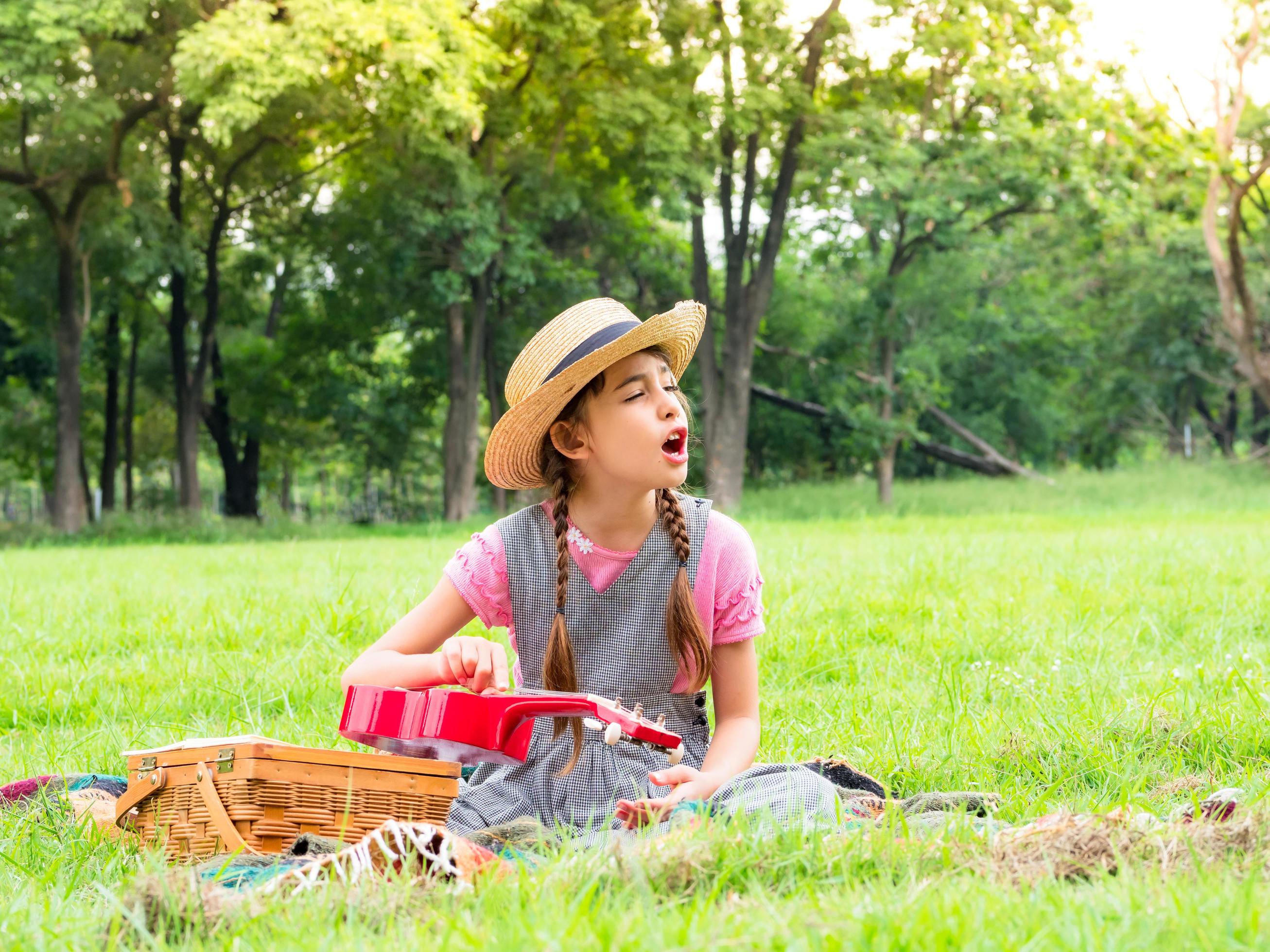 The girl sits on the grass and learns to play the ukulele, learning outside of school in the nature park Stock Free