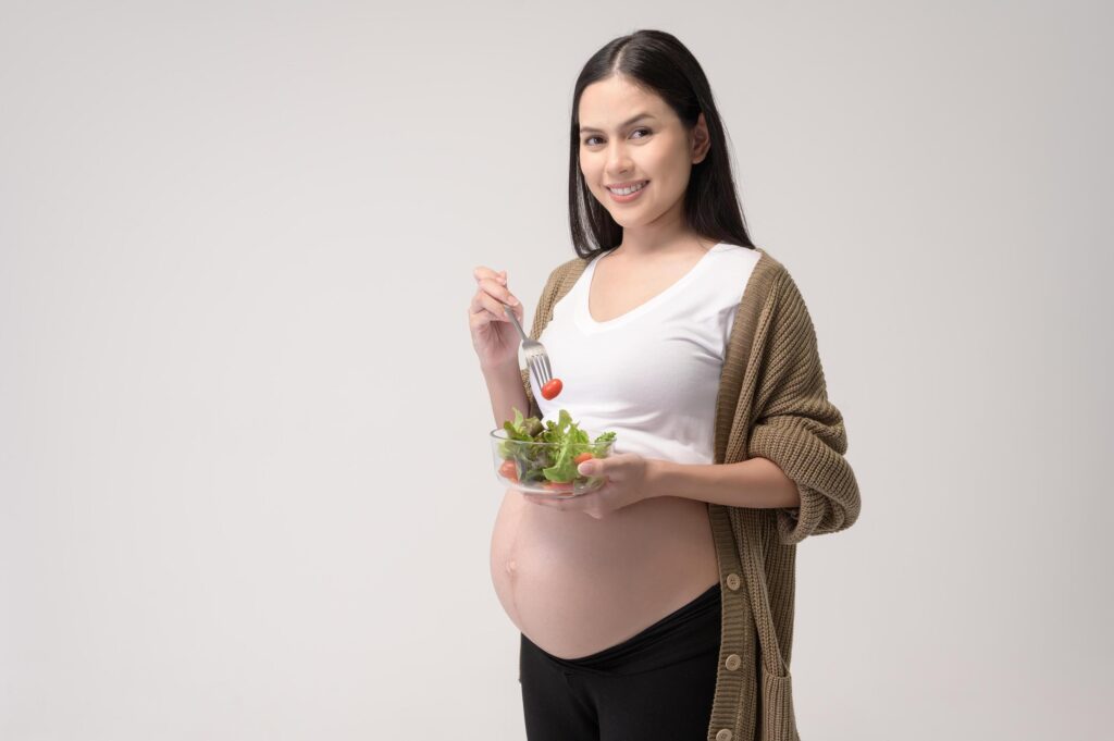 Portrait of Beautiful pregnant woman eating salad over white background studio, health and maternity concept Stock Free