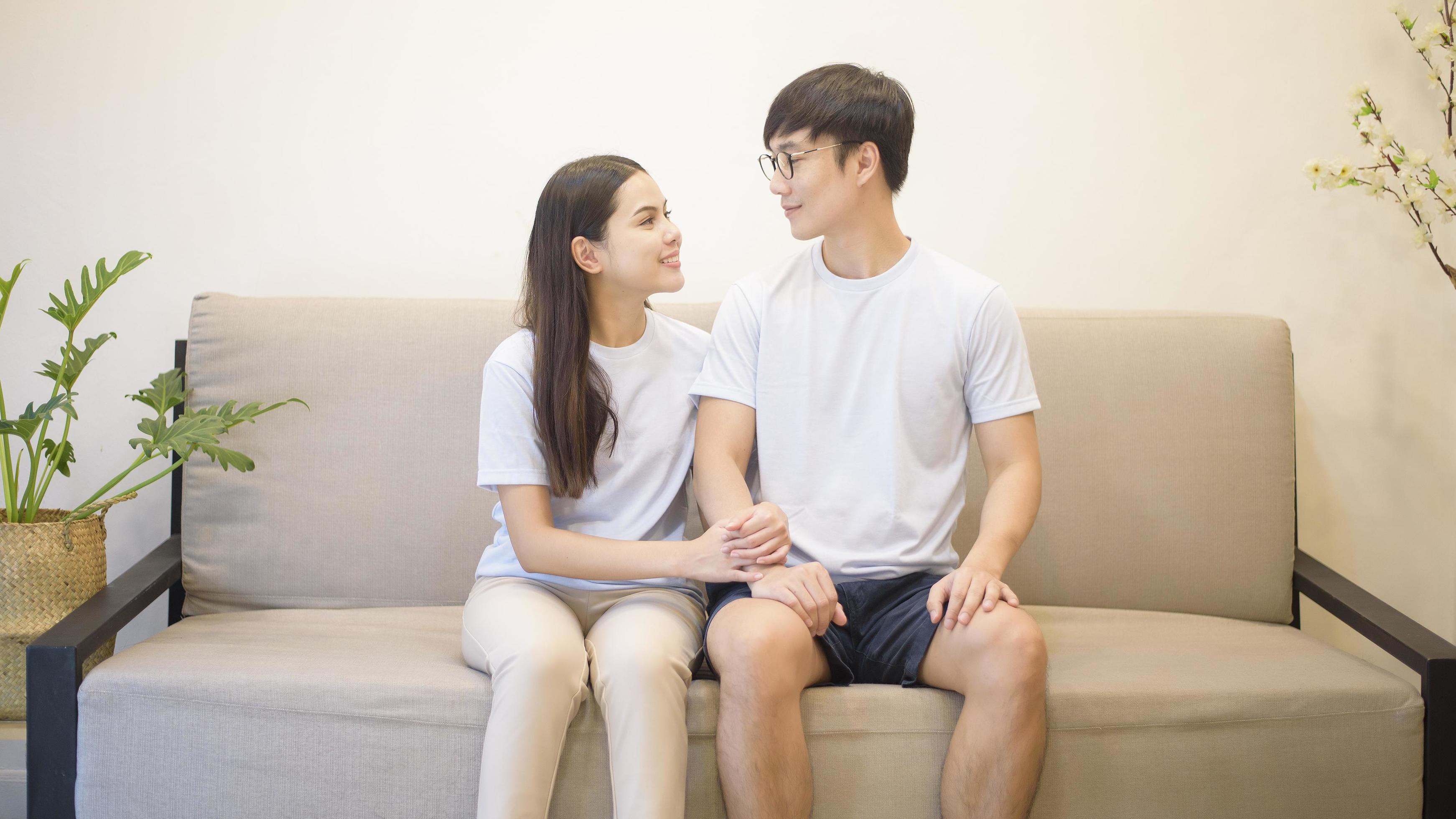 a happy couple wearing blue shirt is sitting on a sofa at home Stock Free