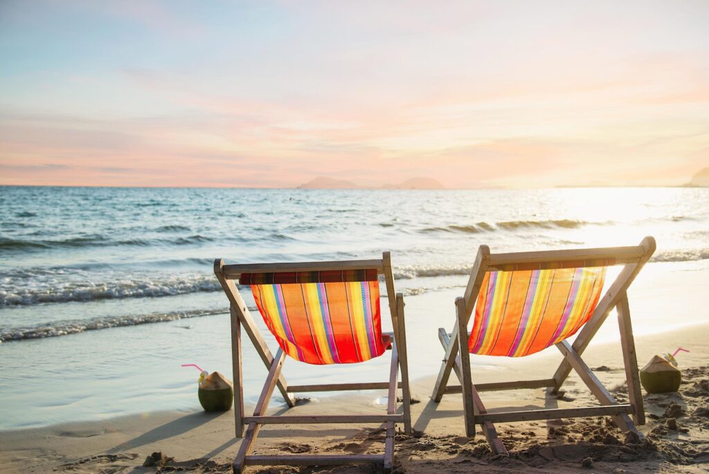 Couple relax chair on sand beach with warm sunset – vacation in beautiful sea nature concept Stock Free