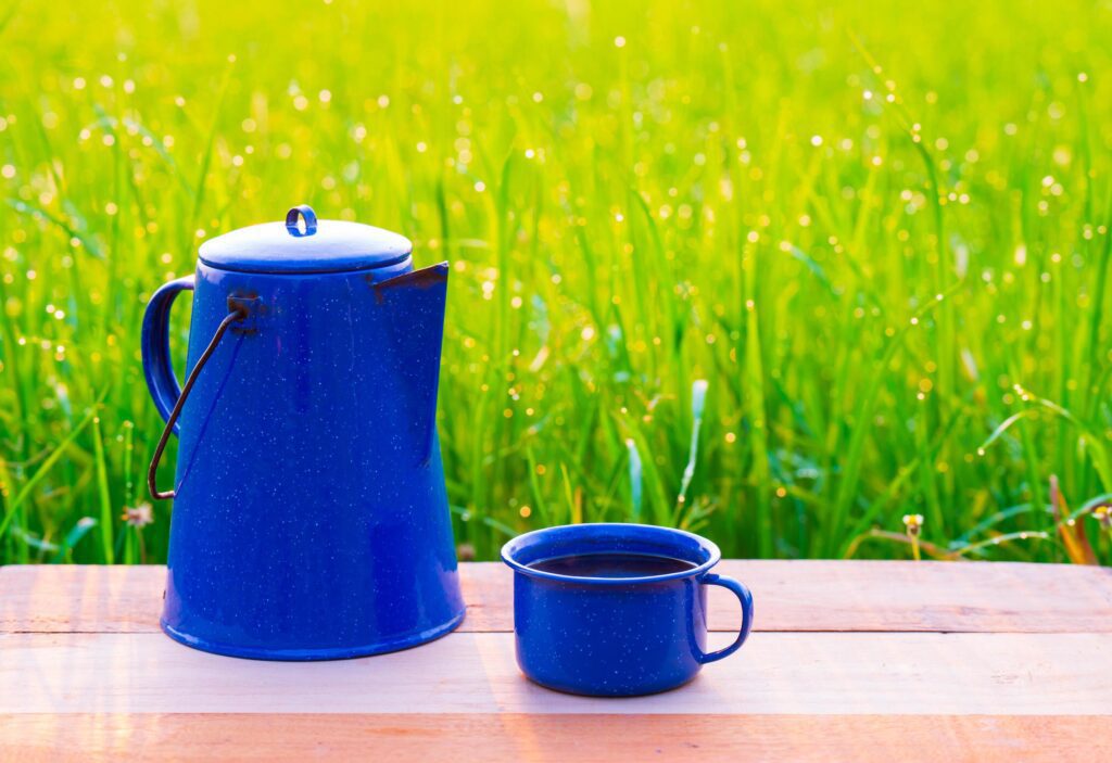 Kettle, blue enamel, and coffee mugs On an old wooden floor, Blurred background of rice fields at sunrise. Stock Free