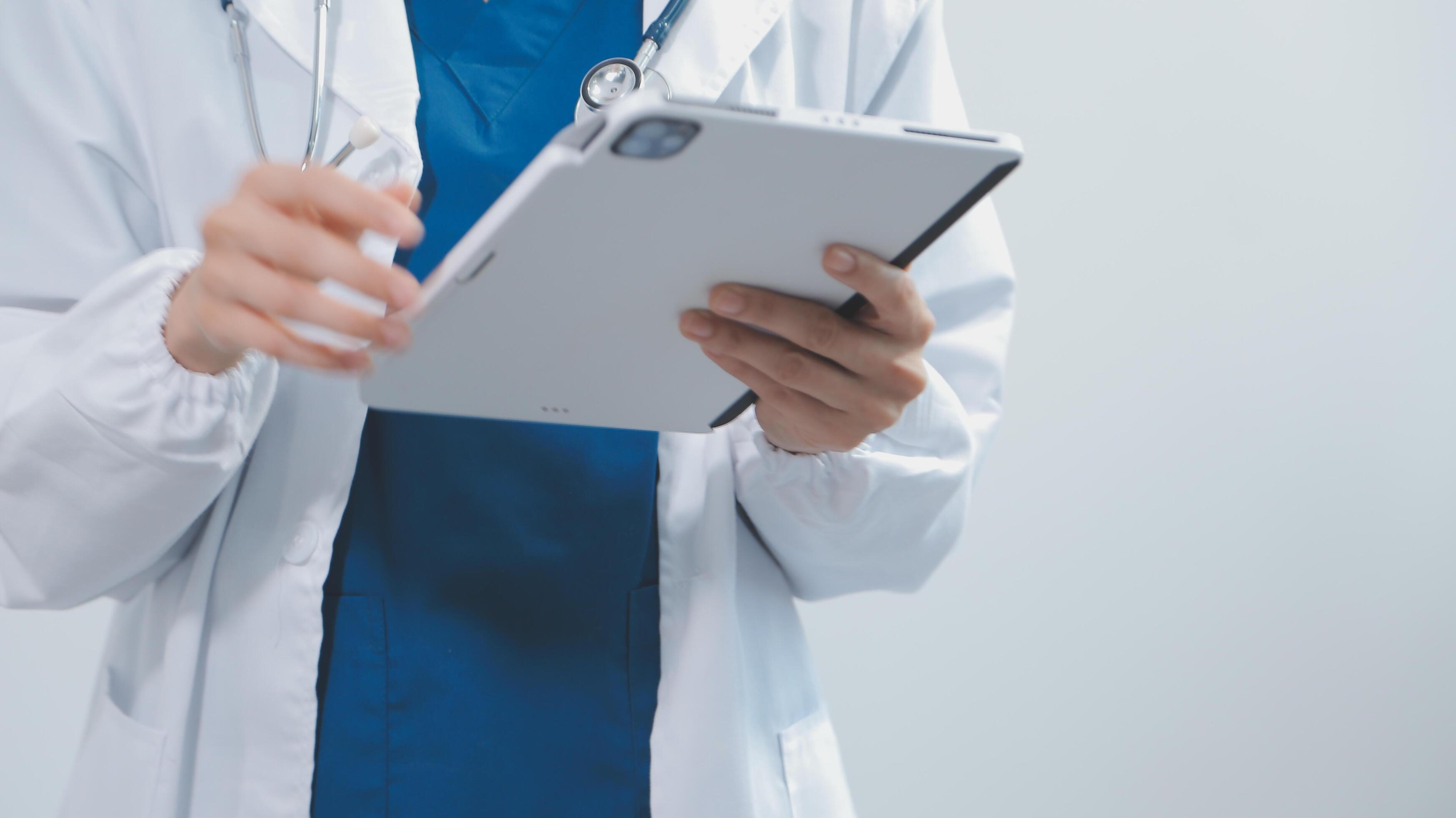 Mature male doctor with tablet pc is giving presentation. Blurred background indoors. Stock Free