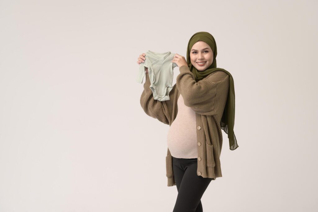 Portrait of Pregnant muslim woman in hijab holding baby cloth over white background studio Stock Free