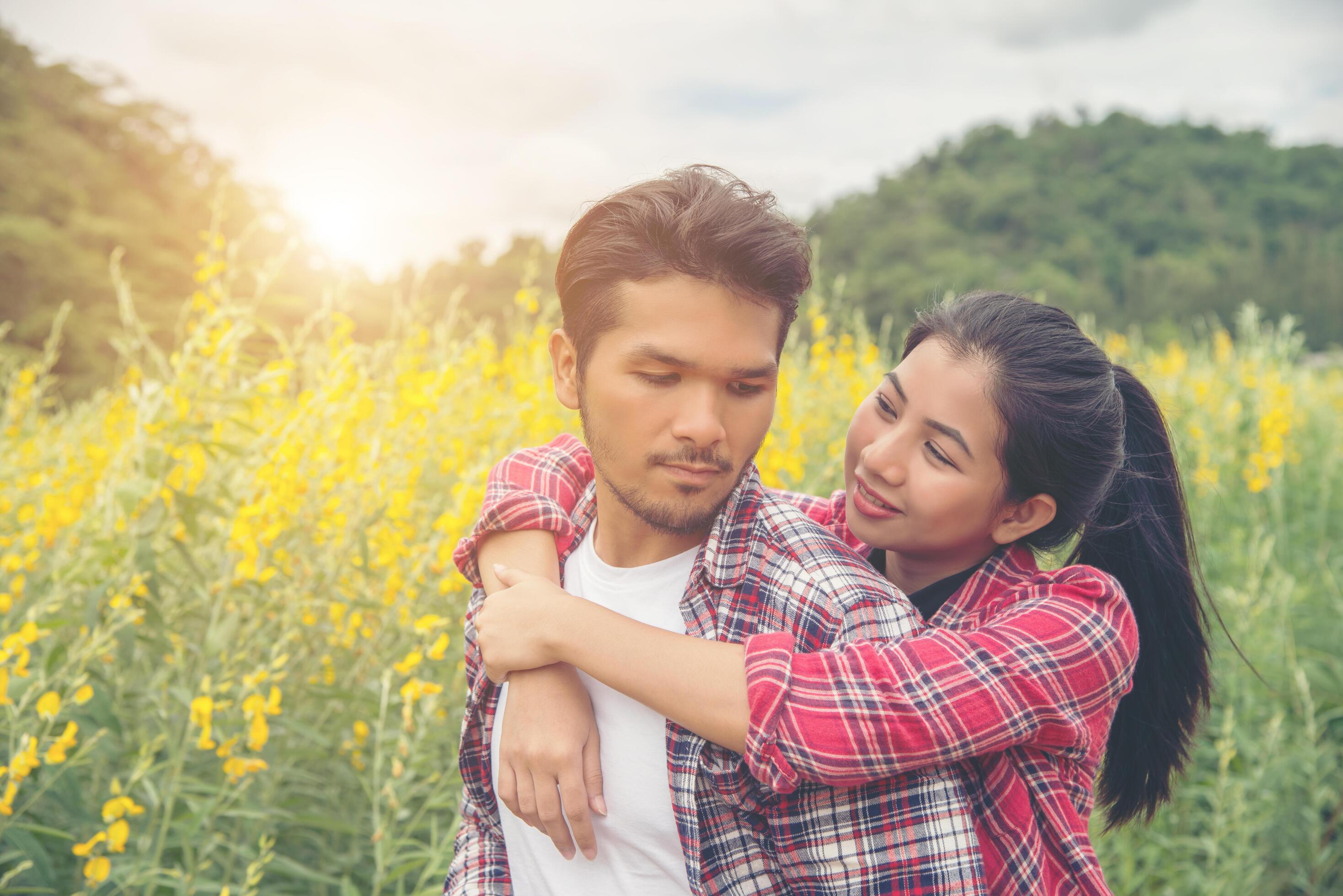 Young hipster couple relaxing in yellow flower field at summer. Enjoying with nature. Stock Free