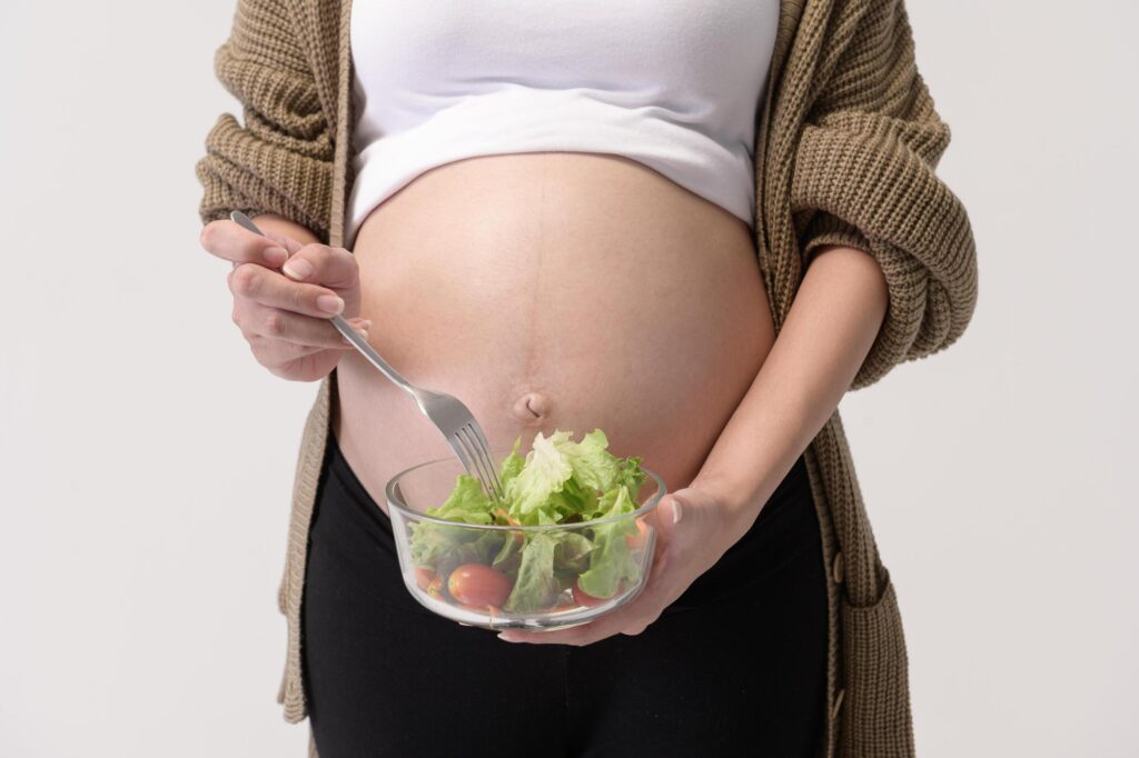 Portrait of Beautiful pregnant woman eating salad over white background studio, health and maternity concept Stock Free