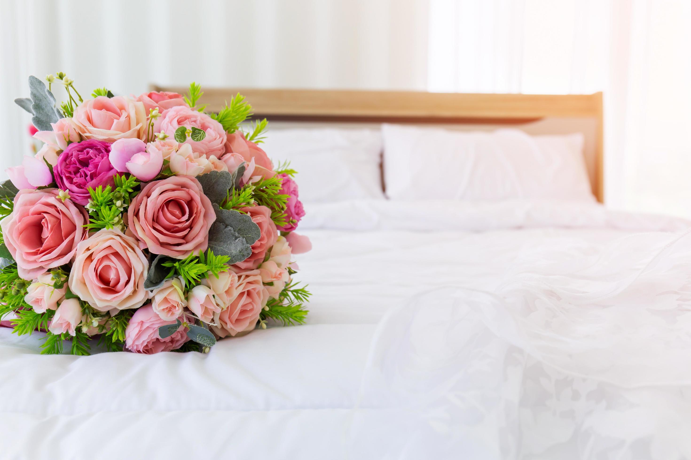 A beautiful bouquet of flowers was laid out on a clean, white bed. Next to the bridal gown were placed together. Stock Free