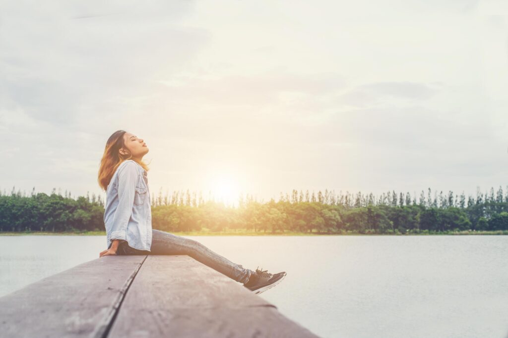 Young beautiful hipster woman sitting on the lake relaxing with fresh air. Stock Free