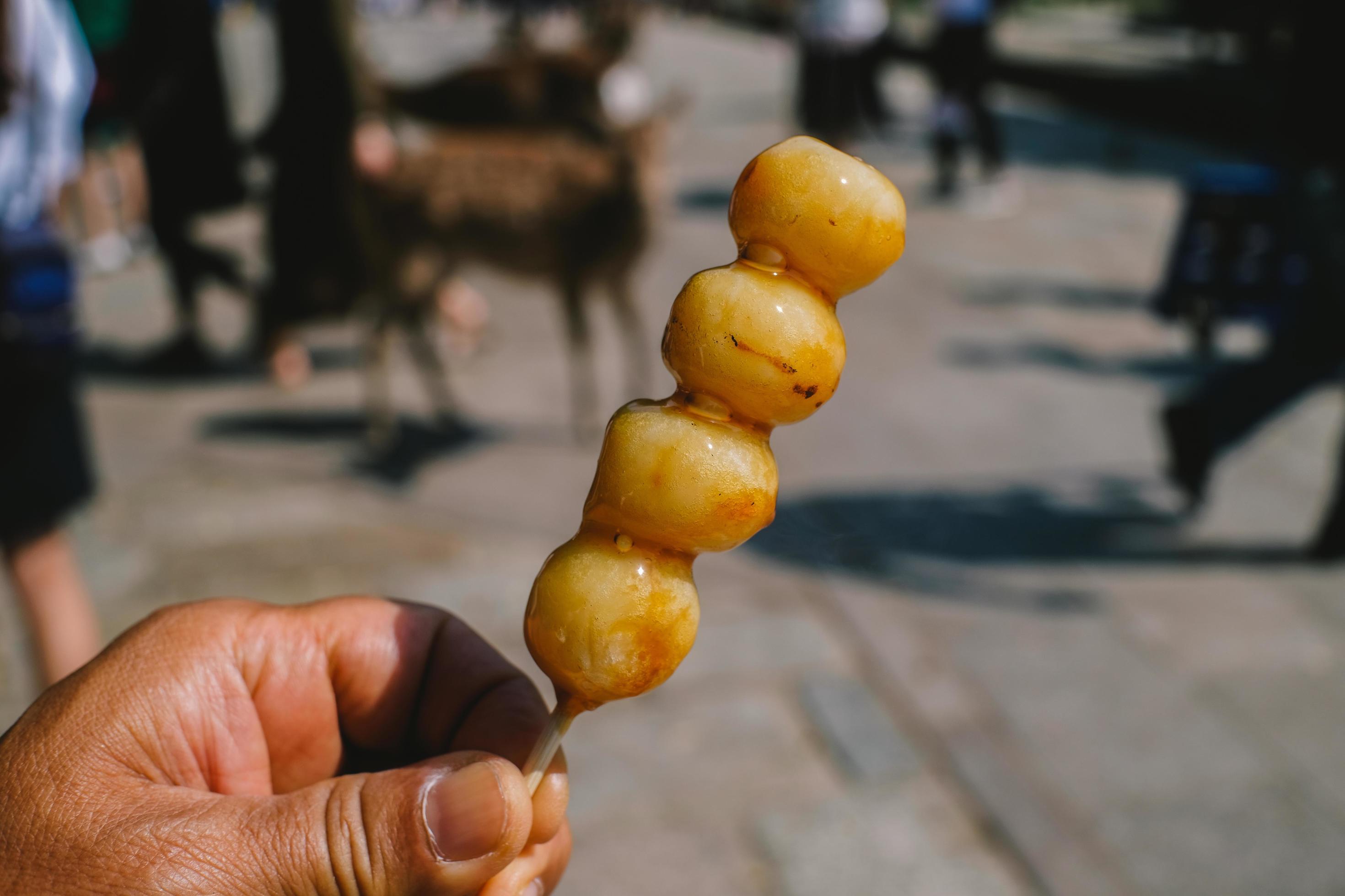 Hand holding Dango on light nature background. Enjoy eating Dango cover sweet soy sauce. Traditional Japanese street food. Stock Free