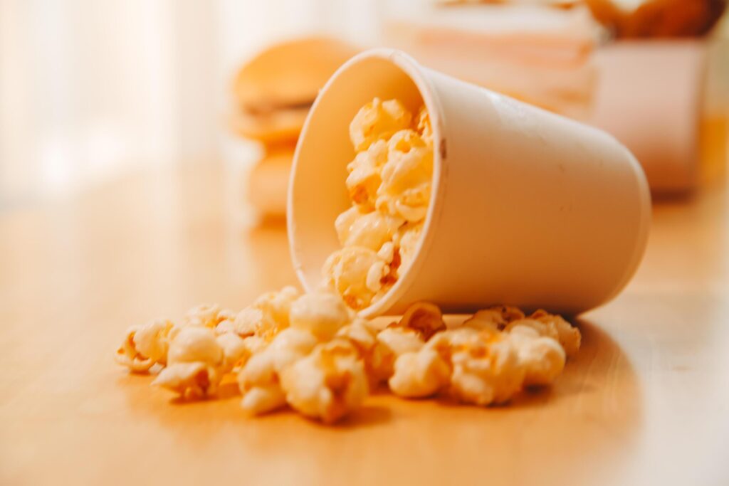 A bucket of popcorn, top-view, warm colors, light brown wooden background, flat lay, daylight macro close-up Stock Free