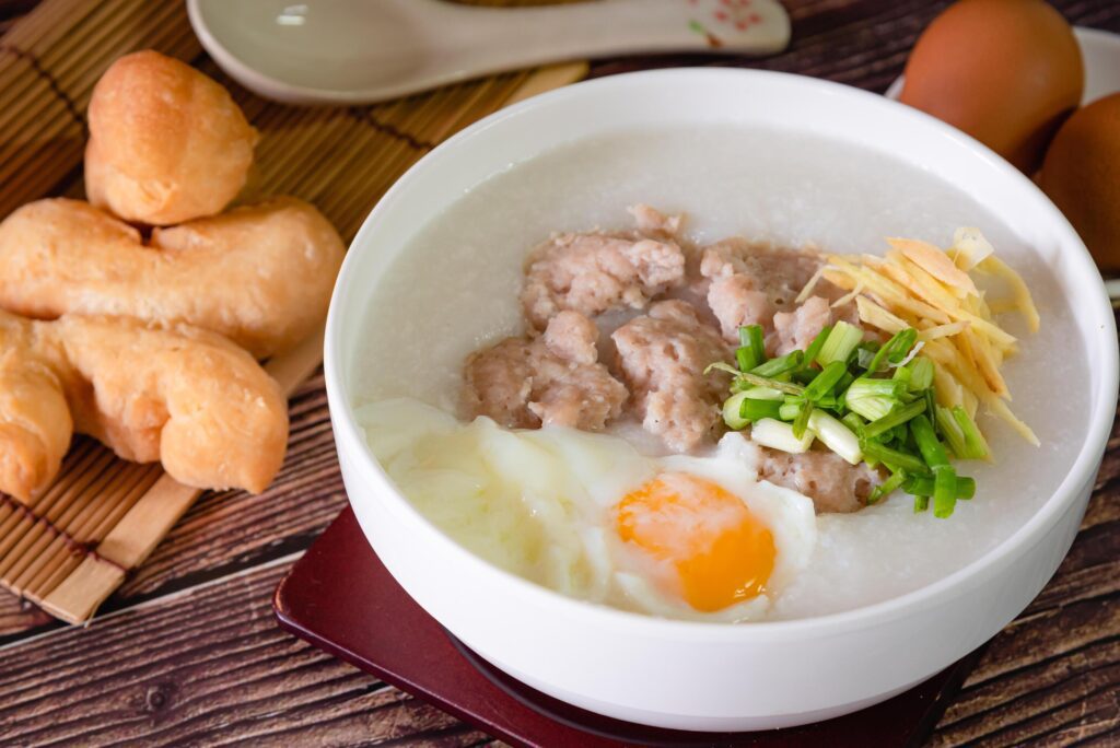 Chinese rice porridge, Congee with pork, egg and vegetable on wooden background Stock Free