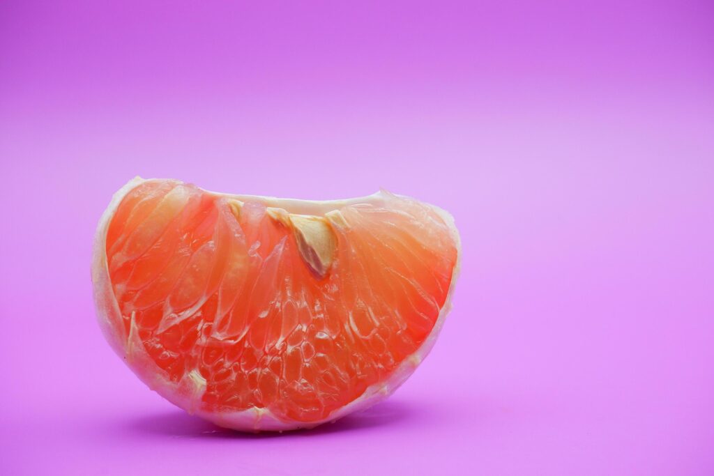 a slice of grapefruit isolated on a purple background. grapefruit that has been peeled until the grain of the orange is visible Stock Free