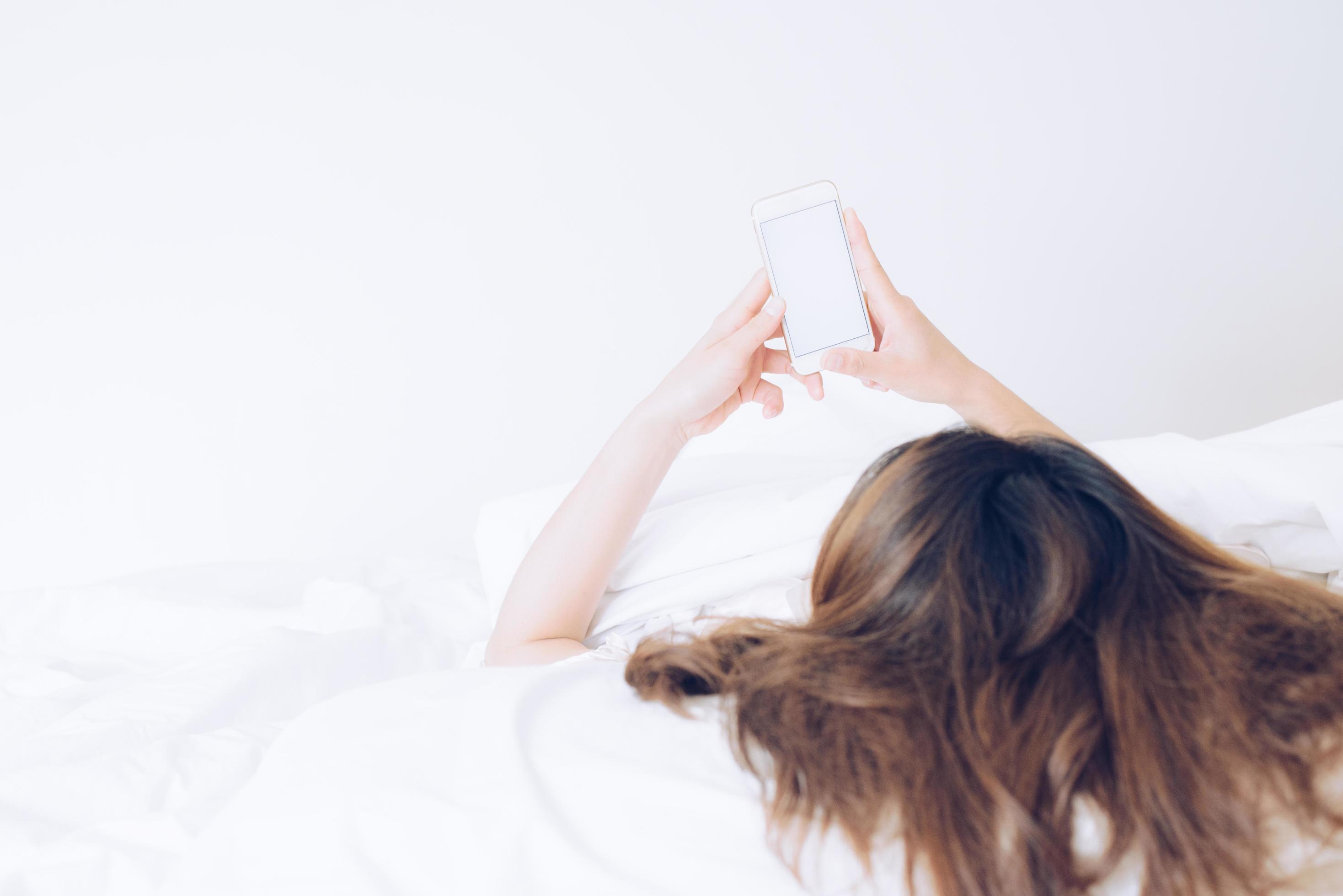 Cropped shot view of Asian woman lying on bed and using her smart phone. Conceptual of woman lifestyle. Stock Free