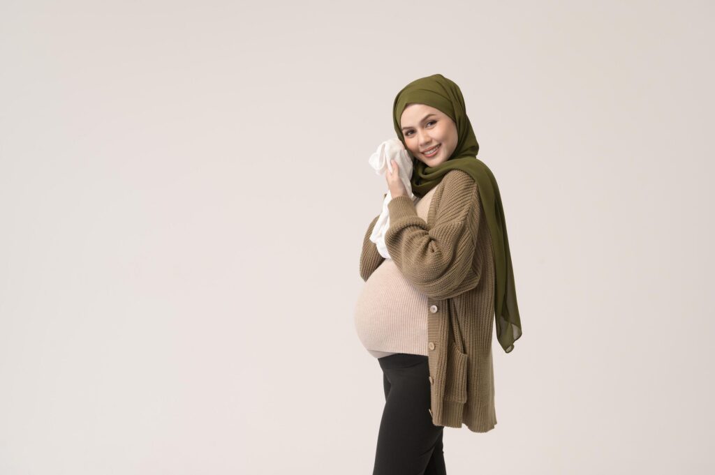 Portrait of Pregnant muslim woman in hijab holding baby cloth over white background studio Stock Free