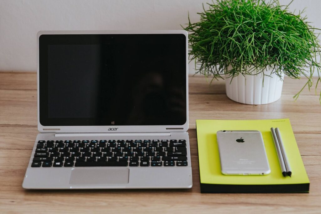 Silver Acer laptop, a white Apple iPhone and a notepad on a wooden desk Stock Free