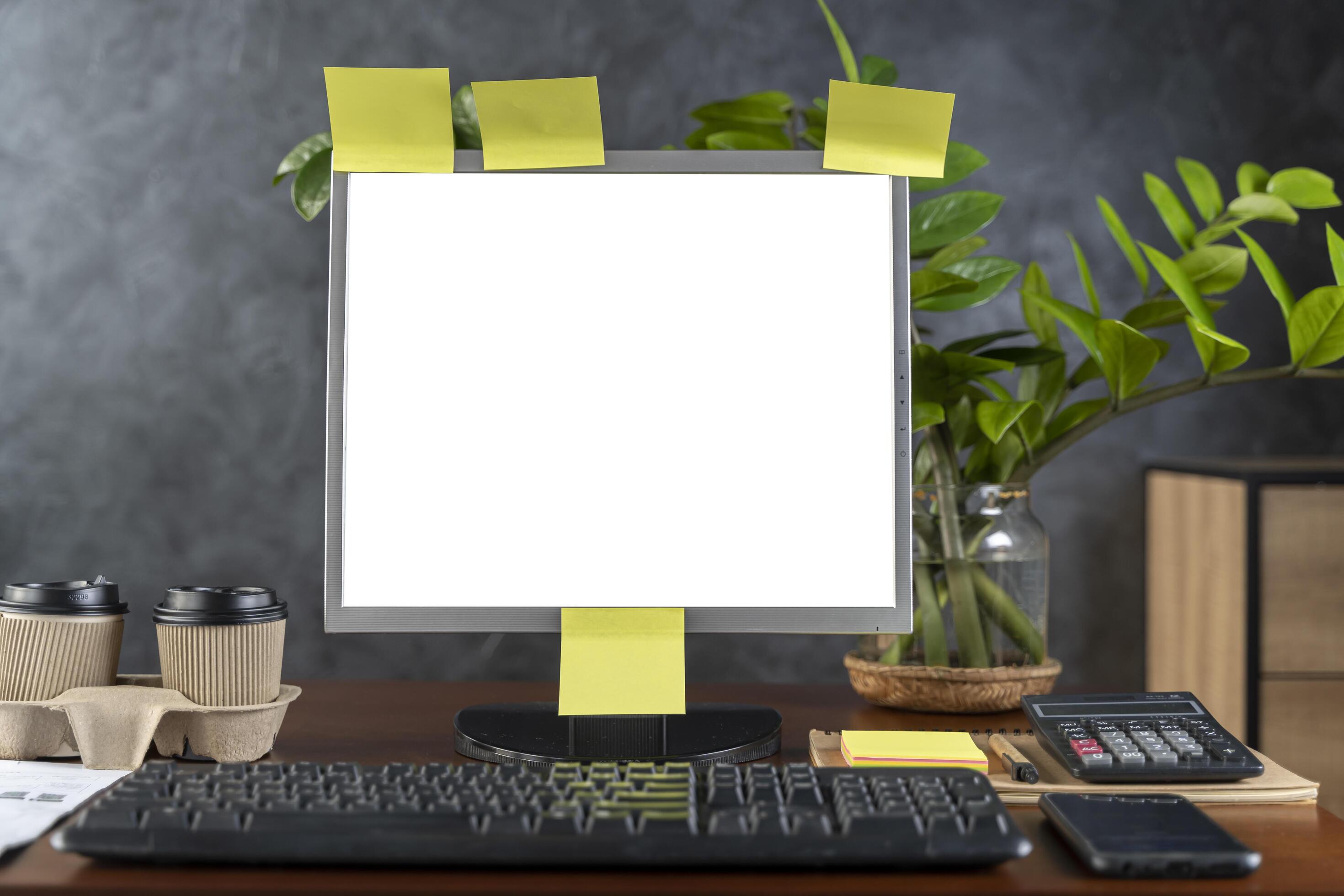 Computer monitor with white blank screen on the business desk with calculator, keyboard at home office over dark wall backgroun. Stock Free