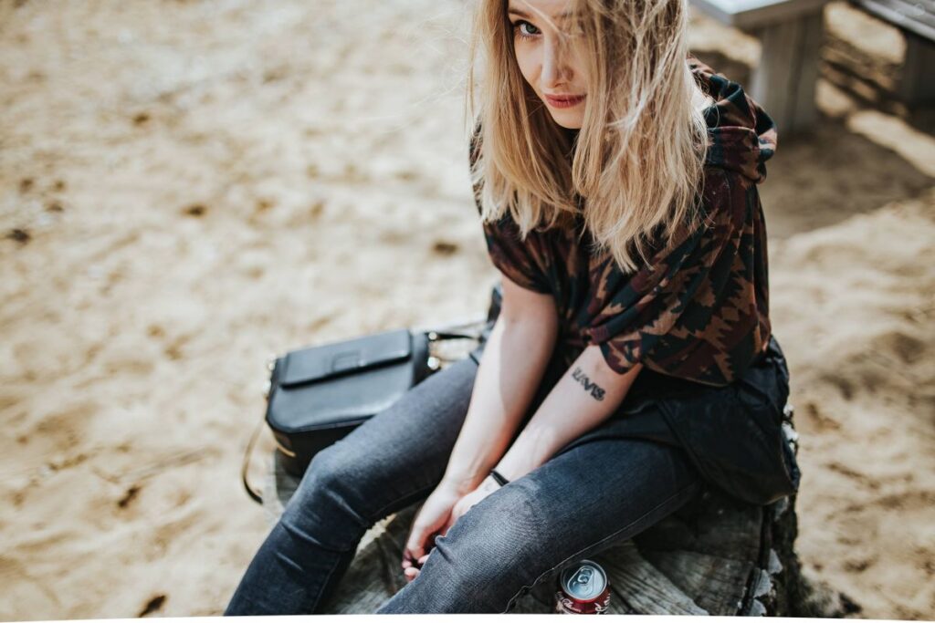 Beautiful blonde woman relaxing with a can of coke on a tree stump by the beach Stock Free