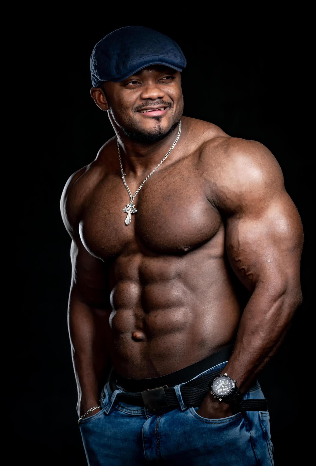 Perfect naked torso of an african american bodybuilder. Man wears blue jeans and denim cap. Black background. Concept photo. Closeup. Stock Free