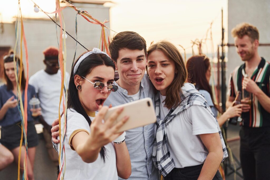 Taking selfie. Group of young people in casual clothes have a party at rooftop together at daytime Stock Free