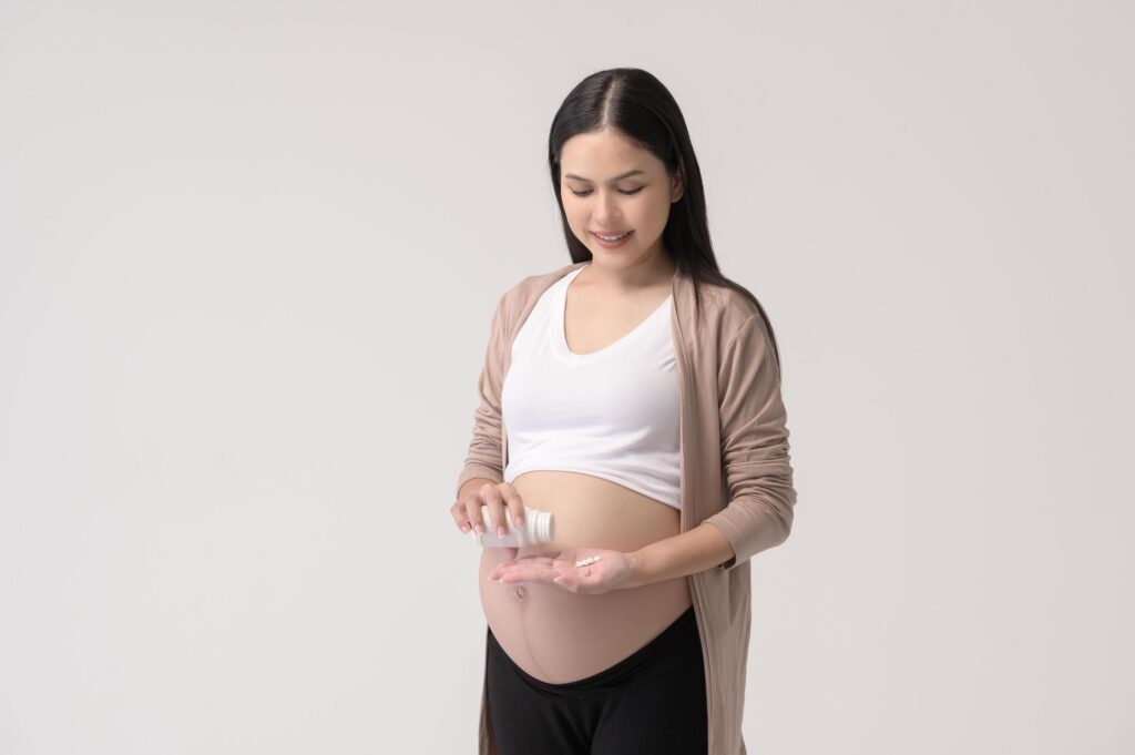 Portrait of Beautiful pregnant woman taking pill and vitamin over white background studio, health and maternity concept Stock Free