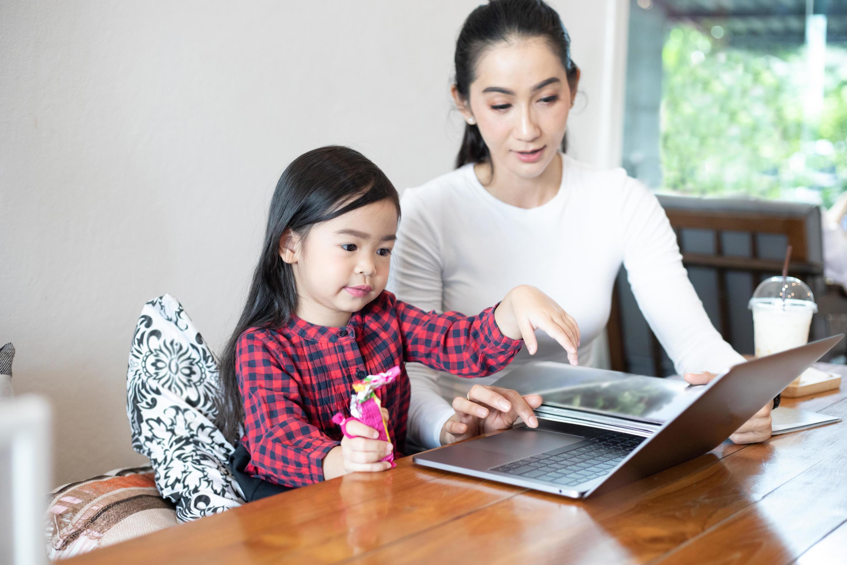 Mom is teaching her daughter to read a book and playing notebook. Stock Free