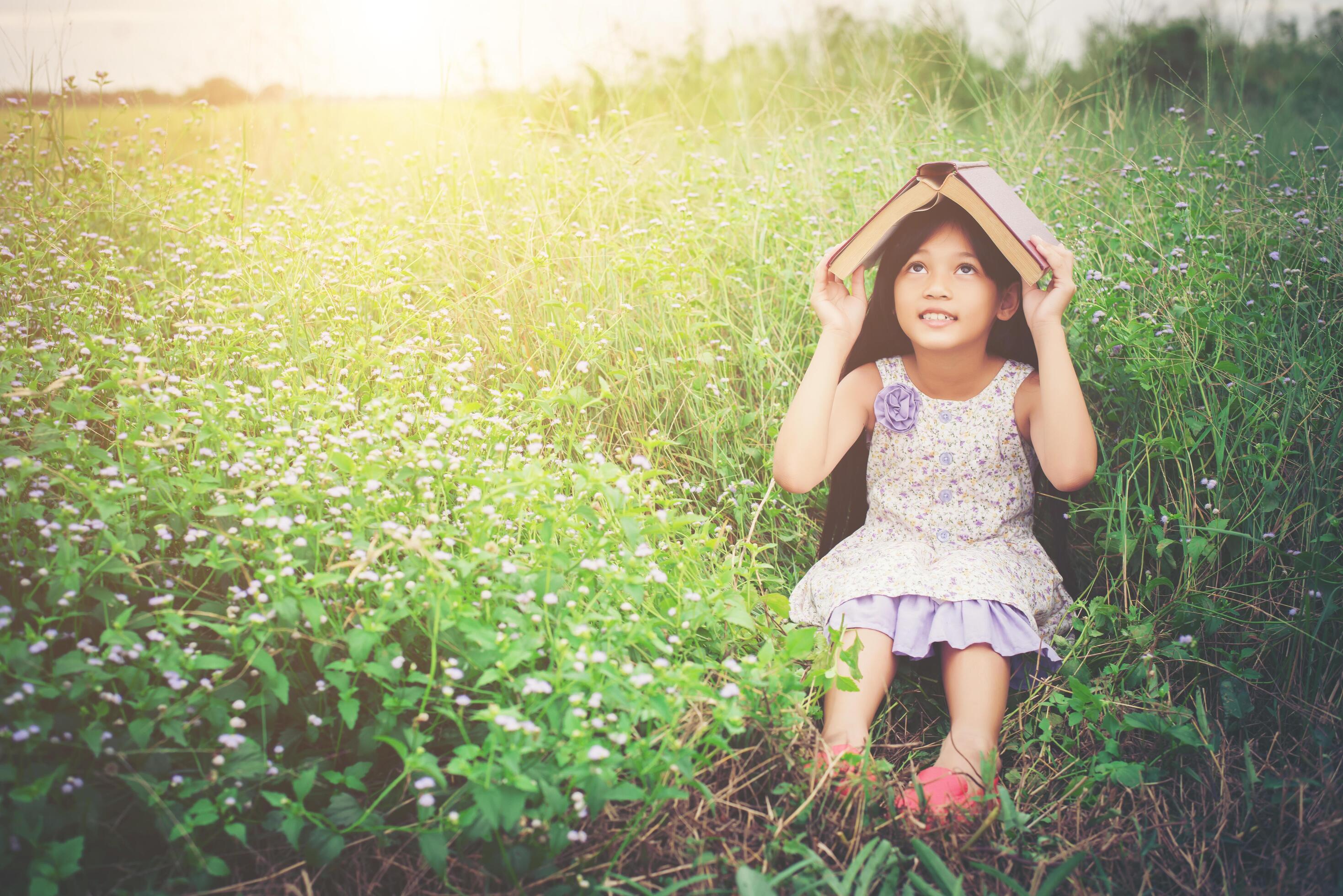 little cute asian girl cover book on her head at nature. Stock Free