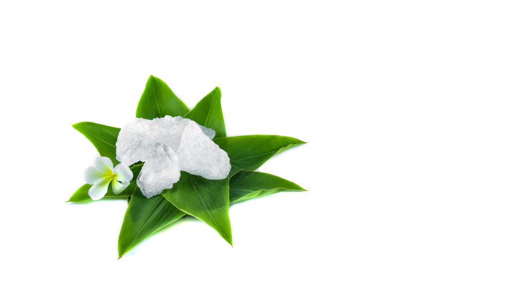 White crystal clear alum cube on green leaf isolated on white background. Stock Free