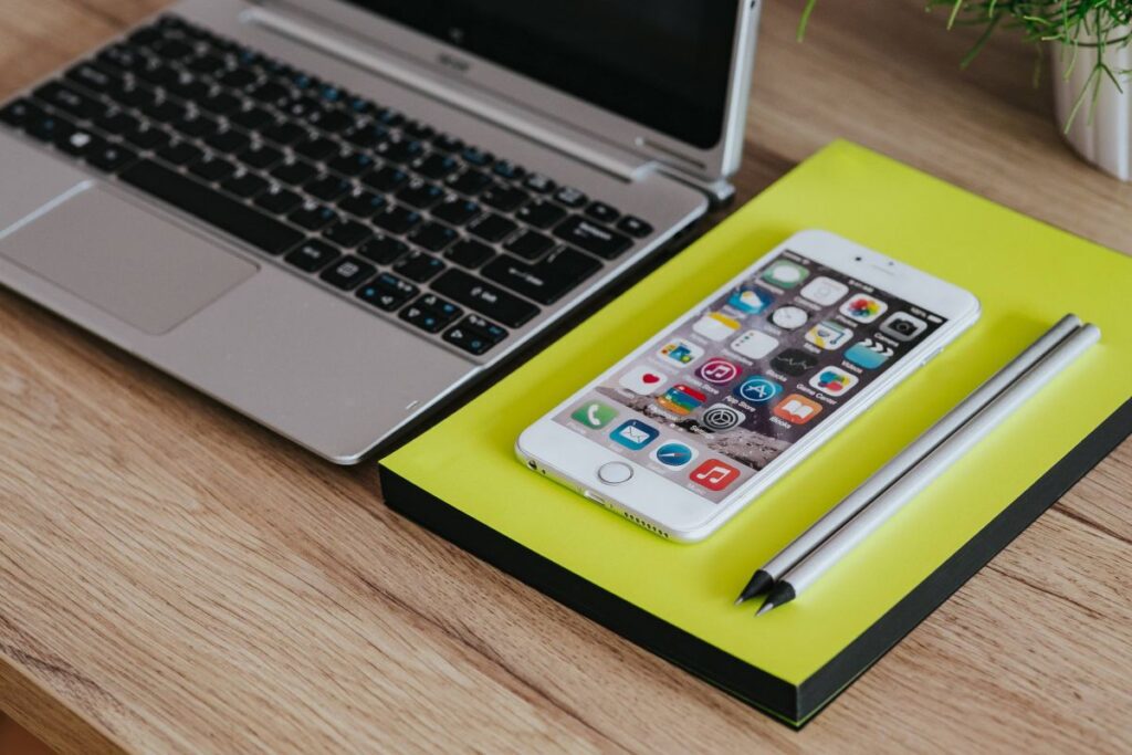 Silver Acer laptop, a white Apple iPhone and a notepad on a wooden desk Stock Free